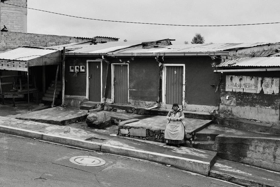a street of low houses with a person sitting on a step, in black and white