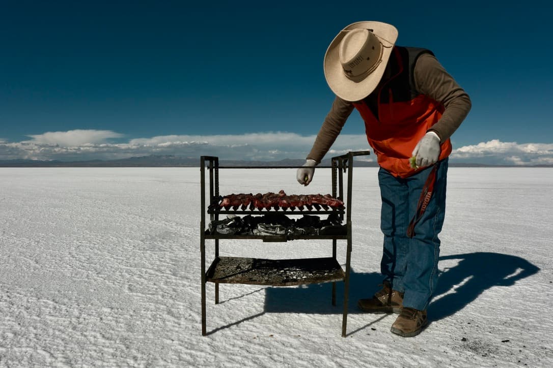 a man in a hat grills meat on a grill on a salt flat