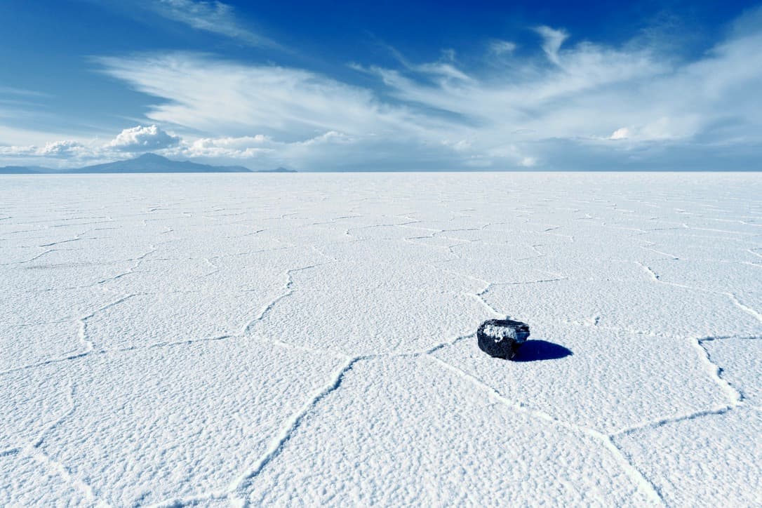 a dark stone on salt crust cracked into hexagons, under a blue sky