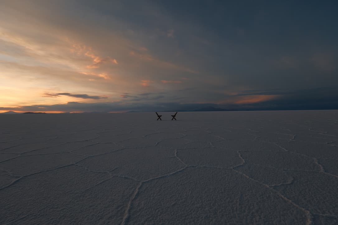 dusk sky over the salt flat, with two small chairs on the horizon