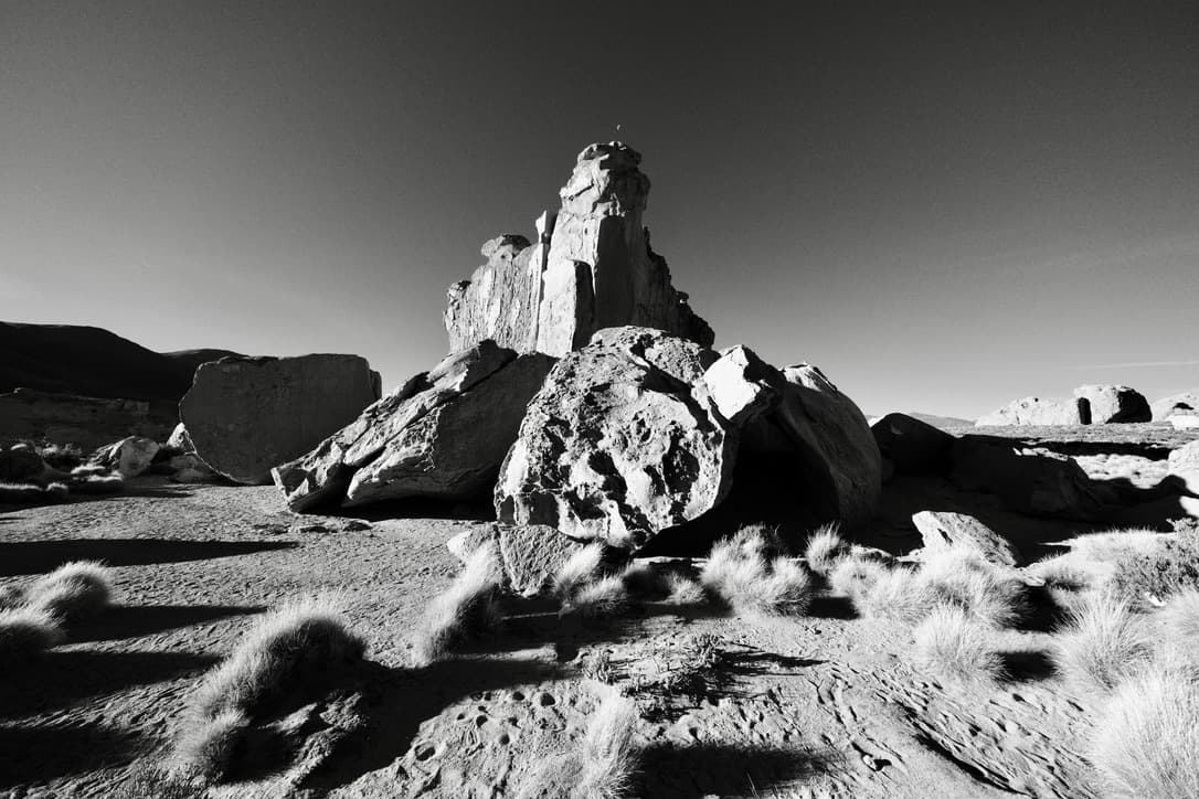 loose boulders and a tall formation under a dark sky, in black and white