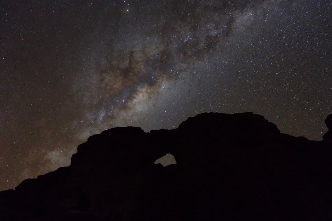 the milky way over the silhouette of a rock with an arch
