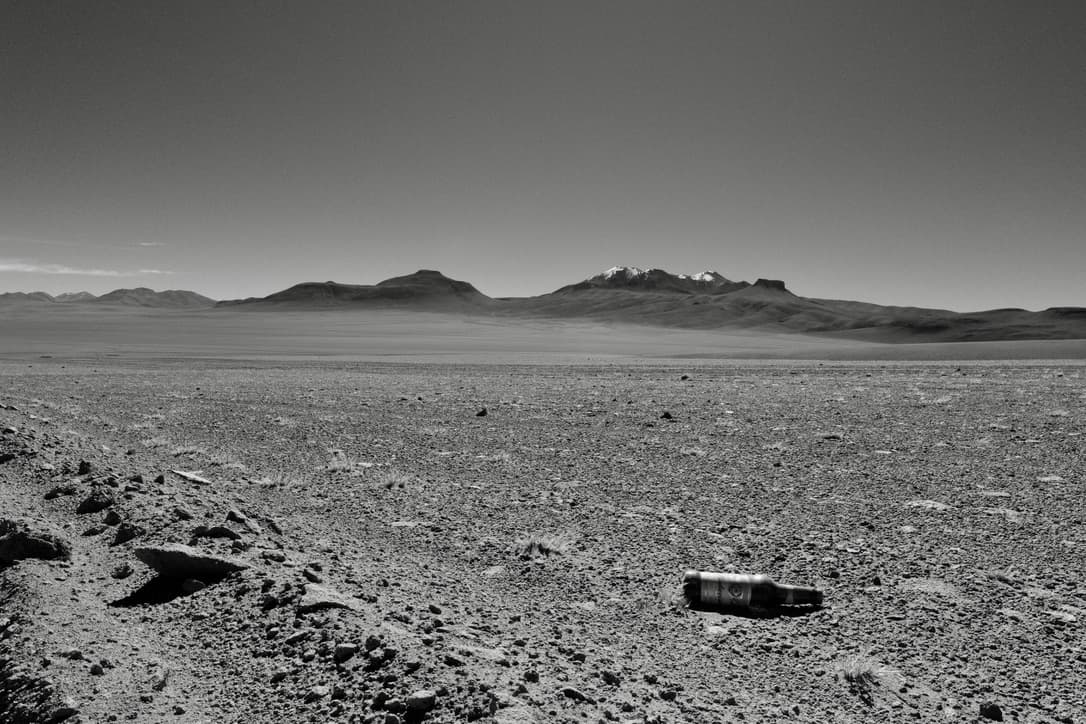 a bottle lying on a stony plain, with snow-capped mountains behind, in black and white