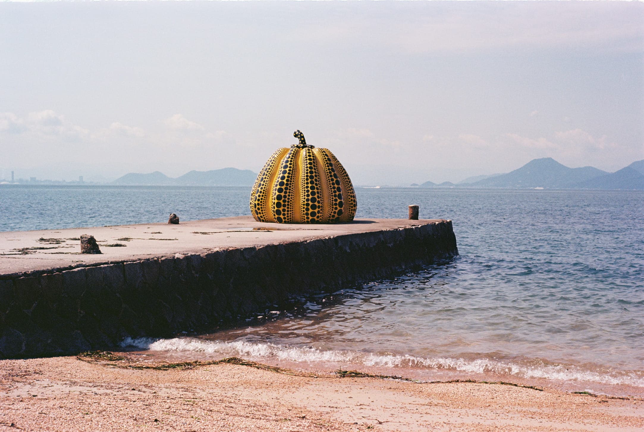 a yellow pumpkin with black dots at the end of a concrete pier, facing the sea