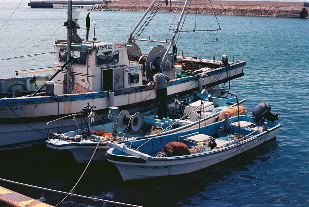 fishing boats moored in a harbor, with a man standing on deck