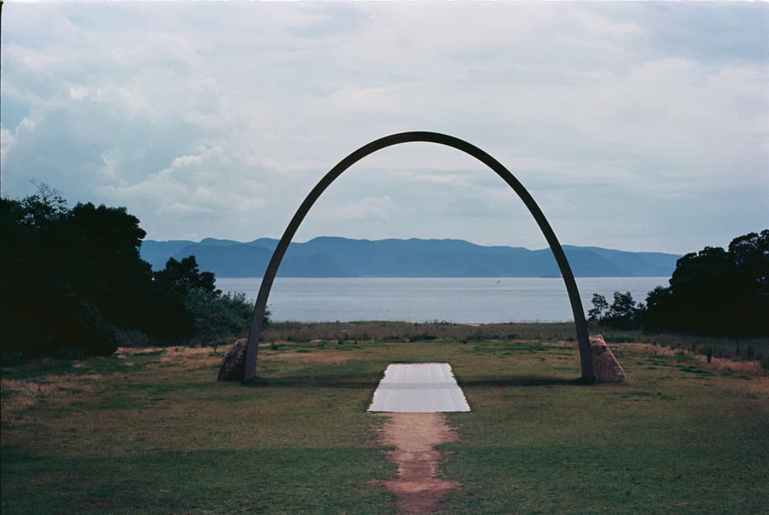 a metal arch on the grass facing the sea, with a white slab on the ground beneath